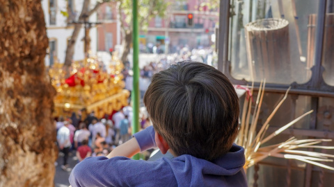 Un niño viendo desde un balcón el cortejo de la Hermandad de la Sed, en Sevilla. E.P./Eduardo Briones