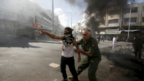 Un oficial de seguridad nacional palestino impide que un chico tire piedras a los soldados israelíes durante los enfrentamientos. Los policías y los palestinos israelíes se enfrentaron el domingo en Jerusalén, donde la violencia en las últi