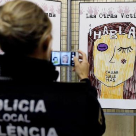 Una agente de la Policía Local fotografía un cartel contra la violencia machista. / EFE