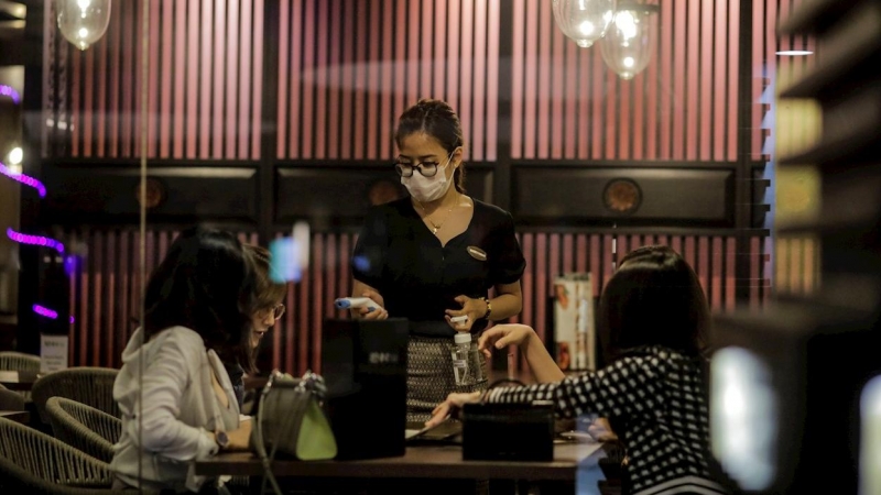 Una camarera con mascarilla atiende a unos clientes en un restaurante de Singapur. EFE/EPA/WALLACE WOON