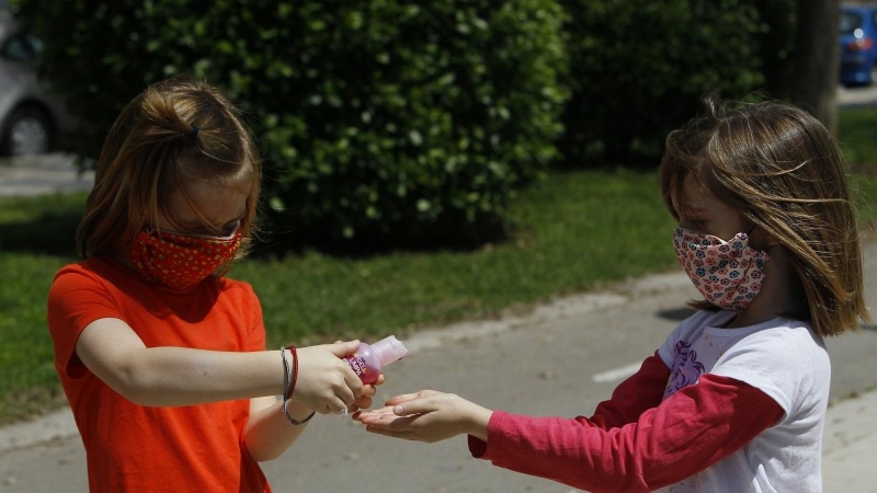 Dos niñas con mascarillas se limpian las manos con solución hidroalcohólica tras salir a la calle.