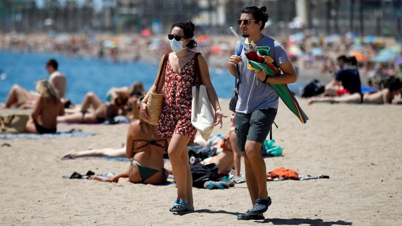 BARCELONA, 24/06/2020.- Dos personas llegan a la playa de la Barceloneta, tras la noche en la que se ha vivido una verbena de San Juan atípica por la pandemia de la COVID-19, en la que las playas de la ciudad han permanecido cerradas para evitar aglomerac