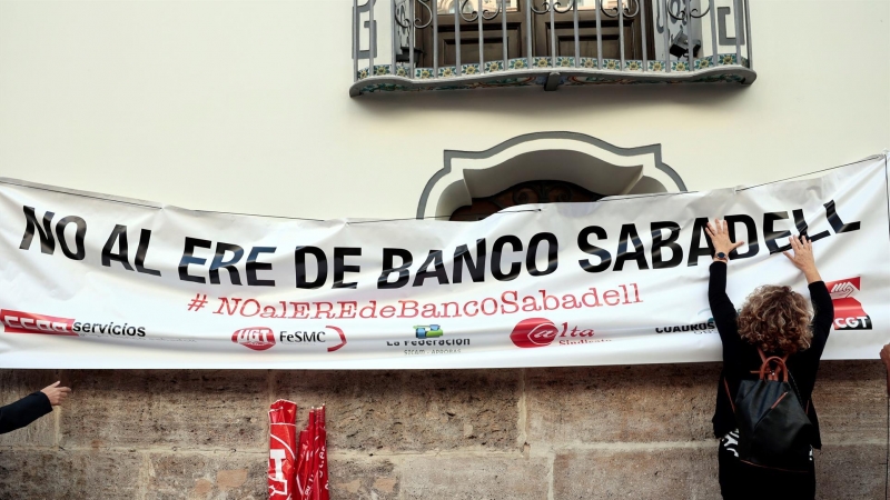 Una persona cuelga una pancarta en la fachada del banco Sabadell en Valencia