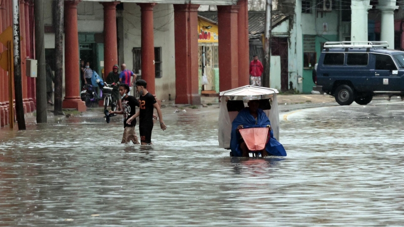 Varias personas caminan por una calle llena de agua, hoy en La Habana