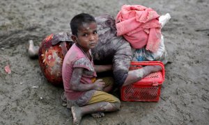 Una niña ronhinyá sentada junto a su madre, que descansa tras cruzar la frontera entre Brimania y Bangladesh. - REUTERS