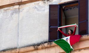 Una mujer luce la bandera italiana desde su ventana para celebrar el 75 aniversario de la liberación italiana, durante el confinamiento decretado por pandemia del coronavirus.- efe