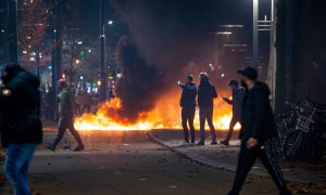 La gente se para cerca de objetos en llamas después de que una protesta  en Róterdam contra la 'política 2G' se convirtiera en disturbios