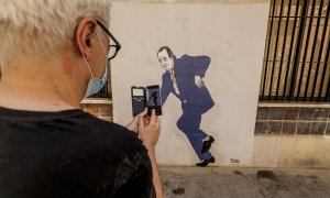 Un hombre hace una fotografía con su móvil al graffiti del rey emérito Juan Carlos I tropezando y a punto de caer, obra pintada en una céntrica calle de Valencia por el artista gallego apodado 'el Primo de Banksy', en Valencia, Comunidad Valenciana (Españ