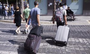 Dos turistas con maletas cruzan un paso de peatones en Sevilla.