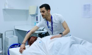 Un col·laborador del projecte europeu QUSTom ajuda una dona a col·locar-se en el llit per a una nova tècnica basada en ultrasons tomogràfics en 3D i supercomputació per a la detecció precoç del càncer de mama, a l'Hospital Vall d'Hebron.