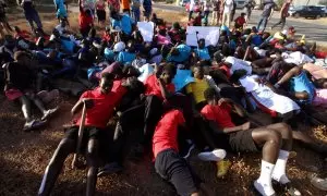 Varias personas migrantes tiradas en el suelo simulan las imágenes de los cuerpos tendidos en el salto a la valla de Melilla, a 29 de junio de 2022, en Melilla (España).