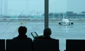 Dos personas esperan sentadas frente a un avión aparcado en la pista del aeropuerto de El Prat, a 19 de enero de 2023, en el Prat de Llobregat, Barcelona.