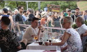 Varios turistas sentados en la terraza de un bar ante el paso de la manifestación organizada por entidades ecologistas, vecinales y sociales, este sábado en Barcelona, para reclamar "poner límites" al turismo en la ciudad.