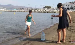 Dues dones omplen ampolles i garrafes del mar a la platja del Port de la Selva