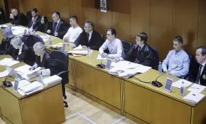 En la imagen, tomada al monitor que sirve la señal del juicio a la sala de prensa, los acusados siguiendo la vista de este lunes.