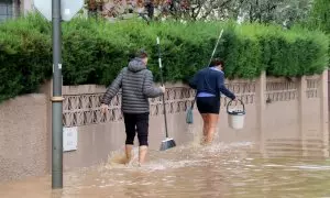 Un home i una dona caminant amb cubells per un dels carrers inundats de la urbanització La Móra de Tarragona