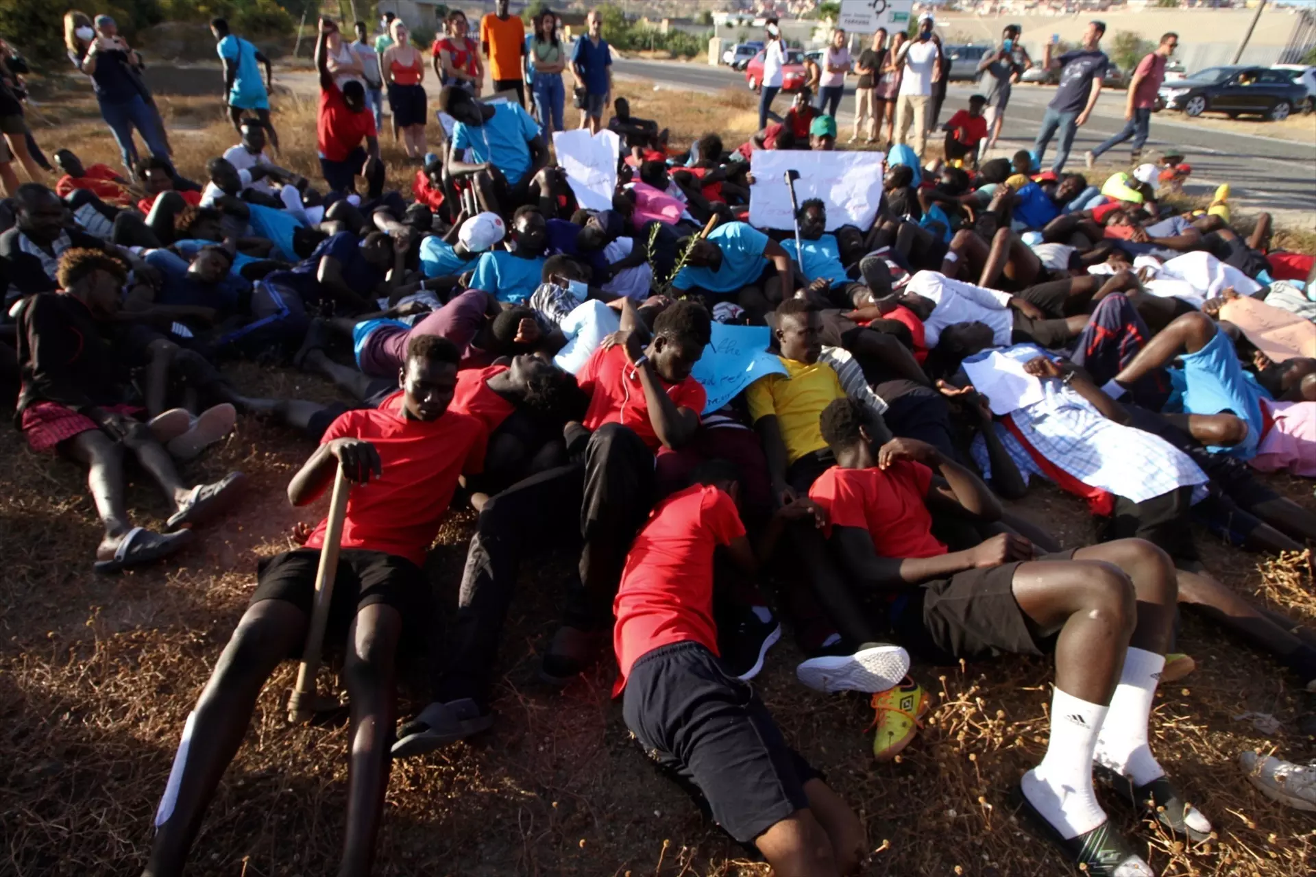 Varias personas migrantes tiradas en el suelo simulan las imágenes de los cuerpos tendidos en el salto a la valla de Melilla, a 29 de junio de 2022, en Melilla (España). — Antonio Ruiz / Europa Press